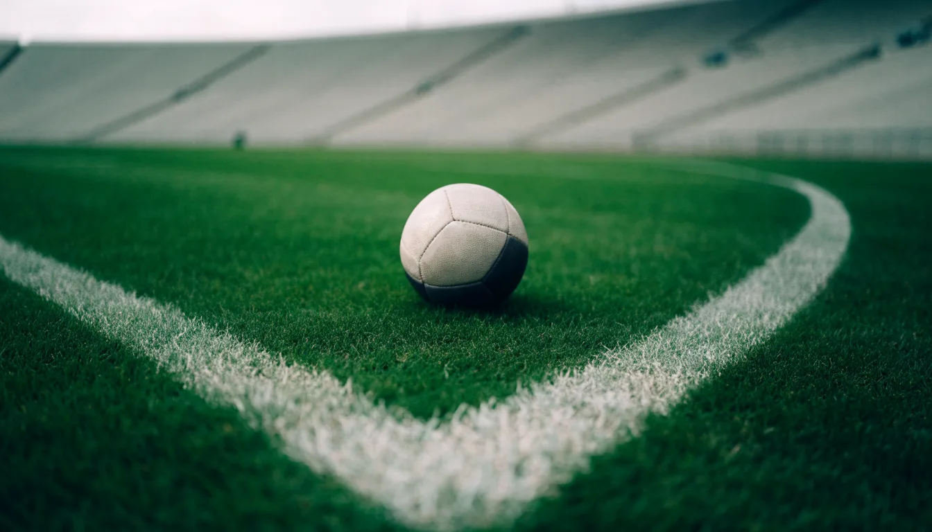 Ein Fußball liegt auf dem Rasen im Mittelkreis, die Kreidelinien führen scharf ins Bild, dahinter verschwimmt eine Tribüne.