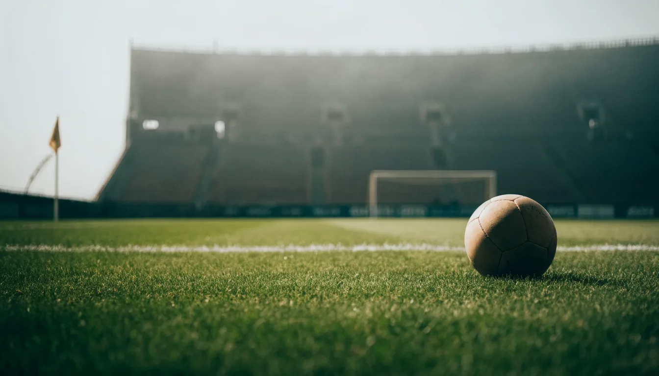Ein Fußball auf einem Rasen, im Hintergrund ein leeres Stadion bei bewölktem Himmel.