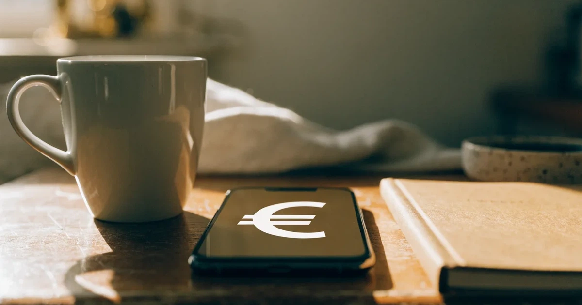 Ein Smartphone mit dunklem Display liegt neben einer Kaffeetasse und einem Notizbuch auf einem Küchentisch.