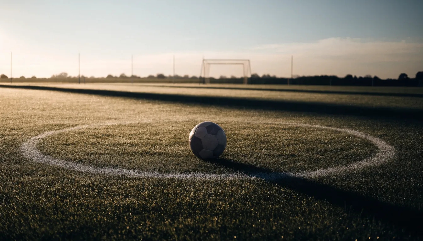 Ein Fußball auf dem Mittelkreis eines leeren Rasenplatzes im frühen Morgenlicht.
