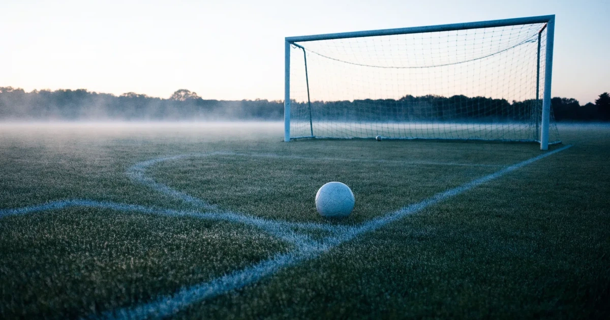 Ein Fußballtor mit Netz steht auf einem leeren Platz im Nebel der Morgendämmerung, der Rasen ist taufeucht.